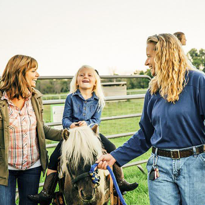 Photo of young child riding horse being led by adults